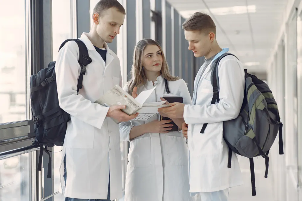 Trois étudiants en médecine, en blouse blanche, échangent leurs notes dans un couloir.