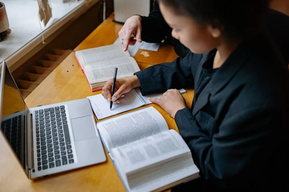 Une personne prend des notes en consultant des livres ouverts.